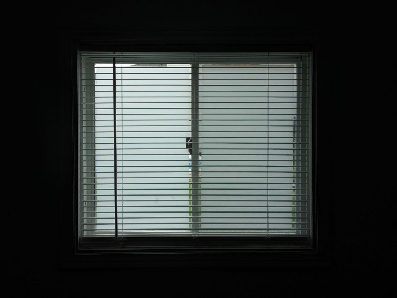 A dimly lit room with closed window blinds casting shadows, creating a serene and secluded atmosphere.